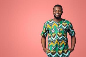 Handsome black man in traditional african clothes smiling over blue studio background, putting hands in pockets, copy space. Cheerful african american guy posing in ethnic colorful clothes photo