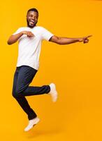 Joyful black millennial guy jumping on air and pointing aside, free space photo