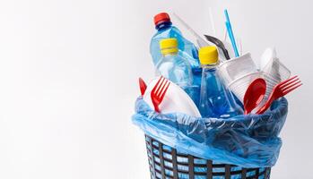 Say no to single use plastic. A black trash can with used plastic items isolated on white background, copy space photo