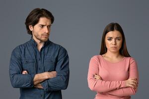Young man looking with offence to his girlfriend after their quarrel, couple having relationship problems, light studio background with free space photo