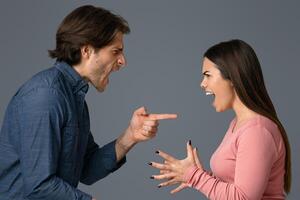 Millennial couple quarreling, shouting and blaming each other, having relationship problems, standing over light studio background, side view photo