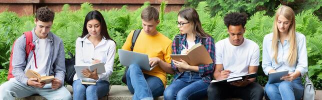 Preparing for lecture. Teens sitting in university campus with books and devices photo