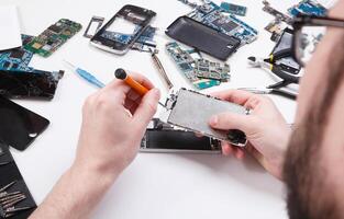 Repairman disassembling smartphone with screwdriver. Technician fixing broken phone, electronics repair service, repairer pov, copy space for text photo