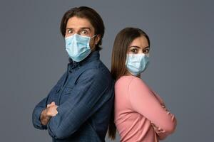 Millennial Couple In Protective Face Masks Standing Back To Back With Scared Face Expressions Over Light Background In Studio, Copy Space photo
