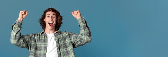 Success and celebration concept. Triumphant young guy showing victory gesture on turquoise background photo