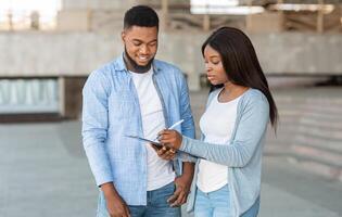 Exit poll concept. Female interviewer making voter survey outdoors after election, talking with young african american guy and taking notes photo