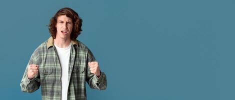 Conflict concept. Furious millennial guy clenching fists on color background photo