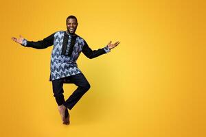 Full size photo of friendly black man dancing over pink studio background, copy space. Cheerful african american guy wearing traditional costume and showing welcoming gesture, studio shot