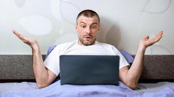 Computer Problem. Displeased Man Using Laptop Shrugging Shoulders Having Issue With Internet Connection Sitting In Bed At Home. photo