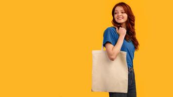 Teen Girl Carrying Eco Shopper Bag Looking Aside At Free Space For Text Posing Over Yellow Background. Studio Shot, Panorama photo