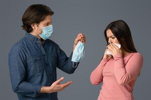 Protective Measures Against Coronavirus. Concerned Man Offering Medical Mask To Sick Girlfriend, Standing Together Over Light Background, Copy Space photo