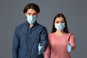 Helping Hand. Young Couple In Protective Masks And Gloves Extending Arms For Handshake At Camera Over Light Studio Background, Free Space photo