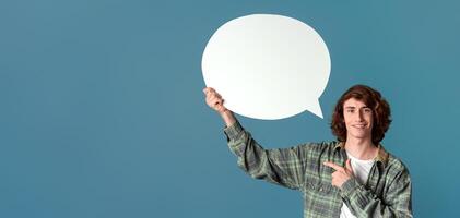 Communication concept. Cheerful curly guy pointing at speech bubble on color background photo