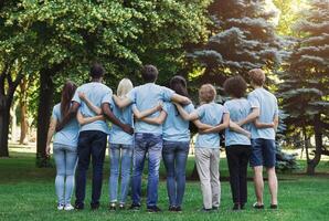 Volunteering, people and ecology concept. Group of volunteers embracing in park, back view, copy space photo