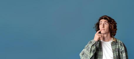 Thoughtful young guy pondering over idea on turquoise background, copy space. Panorama photo