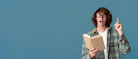 Education concept. Surprised young guy reading book and pointing up on turquoise background photo