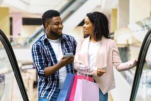 First Meet. Handsome Black Man Introducing With Beautiful Woman In Shopping Center, Asking Her Phone Number While Riding Escalator Together In Department Store, Woman Smiling In Return, Free Space photo
