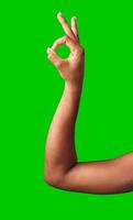 A hand making a gesture with a green background during daylight photo