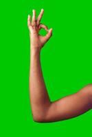 A hand making a gesture with a green background during daylight photo
