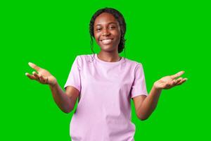 A young woman in casual attire smiles playfully with hands raised in a questioning gesture against a bright green background photo