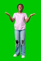A young woman in casual attire smiles playfully with hands raised in a questioning gesture against a bright green background photo