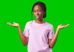 A young woman in casual attire smiles playfully with hands raised in a questioning gesture against a bright green background photo