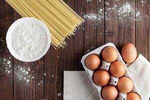 Raw pasta spaghetti with eggs and flour on wooden table. photo