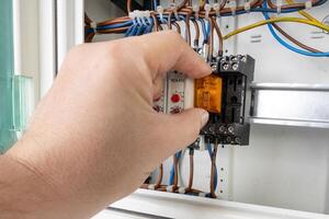 Close up of a hand inserting an electrical relay into a control panel with visible wiring and components. photo