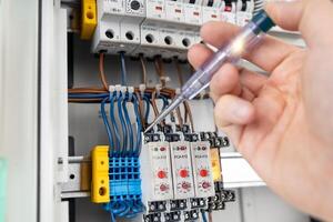 Electrician Testing Electrical Connections with Voltage Tester in Control Panel photo