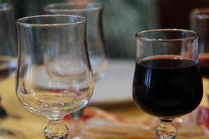 two glass wine glasses. one full of red wine, the other empty. in a bar where people are drinking photo