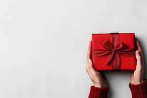 Hands presenting red gift box with sparkling bow on grey backdrop photo