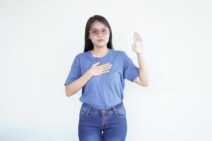 Beautiful Asian woman places her hand on her chest, making a sincere gesture of an oath or promise against a white background photo