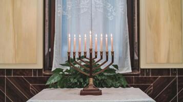 A traditional Hanukkah menorah with nine lit candles stands on a table by a window. Jewish holiday photo