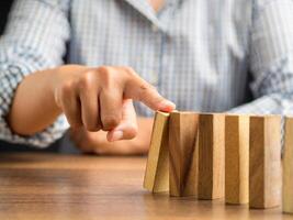 Risk and strategy in business concept. Close-up of hand pushing a wooden block on a line of dominos while sitting in the office photo