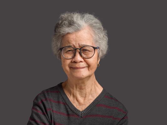 Portrait of a senior woman with short gray hair looking at the camera with a smile while standing on gray background