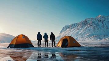 Three people stand in front of tents on an ice covered lake video
