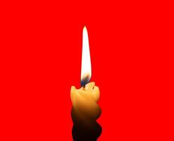 A single burning candle flame or light glowing on a small spiral white candle isolated on red background with clipping path photo