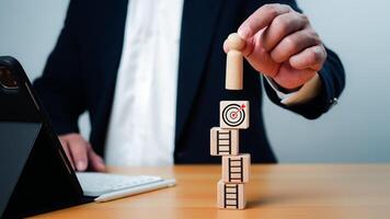 Businessman hand putting wooden doll on wooden cube block and printing target icon, Setup challenge achievement objective in business and life concept, Ladders step for target and goal concept. photo