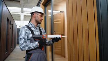 A worker is applying polyurethane foam to fill gap between sash and window frame in prefabricated modular house video