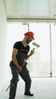 Funny builder dances and sings with long handle roller brush at construction site. Vertical video