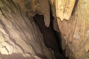 The cave is dark and has a lot of rock formations. The walls are covered in dirt and the ceiling is made of rock. photo