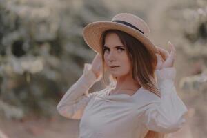 Woman with straw hat stands in front of vineyard. She is wearing a light dress and posing for a photo. Travel concept to different countries photo