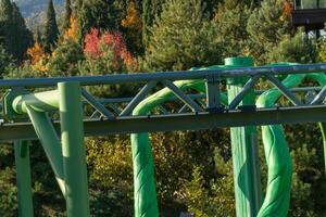 Rollercoaster Track Green Trees Fall - A close-up view of a green rollercoaster track winding through a forest, with fall foliage visible in the background. photo