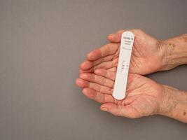 Senior woman hands holding Covid-19 Positive test result with SARS-COV-2 Saliva Antigen Rapid Test Kit photo