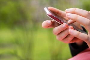 Closeup of a hand holding a mobile phone an outdoor setting. Teenager girl using smartphone, texting or browsing. Mobile technology in daily life. Modern lifestyle. Selective focus. Copy space photo