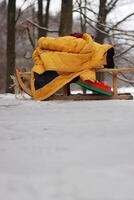 Clolseup of a wooden sled with a warm yellow jacket on a snowy ground in the woods, depicting a winter scene and peaceful retreat into a snow-covered forest. Copy space photo