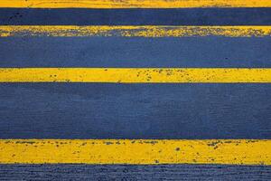 Closeup of a textured asphalt road with weathered yellow stripes on a rough gray pavement, great for use in street photography, urban design, or traffic-related visuals. Copy space photo