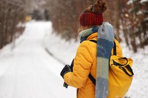 Winter scene with a young woman dressed warmly in a yellow jacket, scarf and red knit headband, walking down a snow covered path through a quiet forest landscape. photo