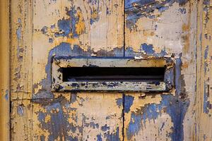Closeup image of a weathered, peeling paint on an old wooden door with a vintage mail slot, perfect for backgrounds, textures, and rustic-themed designs. Copy space photo