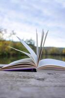 Open book with pages flipping in the wind. Reading on the lake wooden dock on autumn day. Learning enjoying tranquility of nature. Peaceful outdoor environment. Selective focus. Blurred background. photo